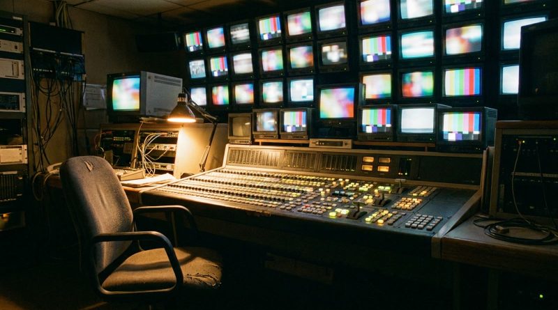 An empty 1980s television master control room with a wall of monitors showing colour bars