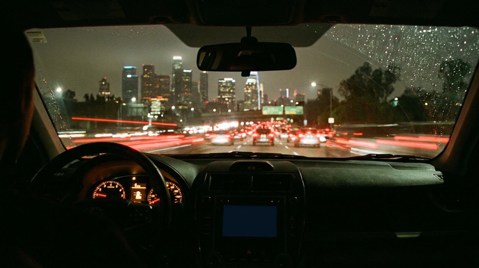 Tráfico nocturno en una autopista de Los Ángeles visto desde el asiento del conductor, con luces traseras rojas que se extienden hacia los rascacielos del centro