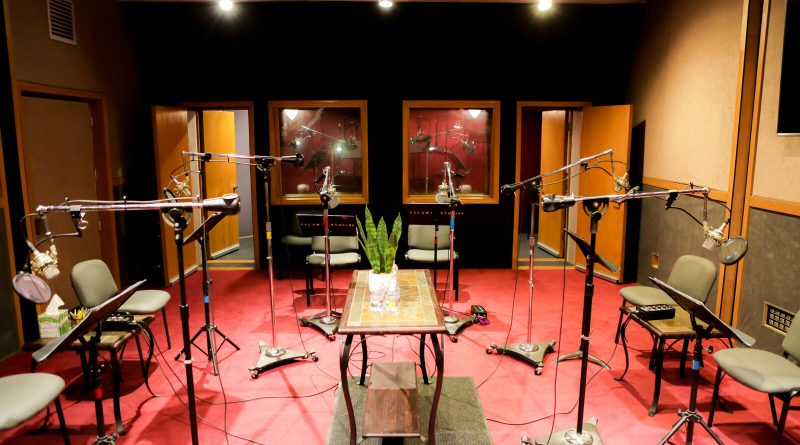 El Studio C de Salami Studios en North Hollywood: una sala de grabación de elenco con alfombra roja, un círculo de micrófonos, atriles y sillas, y ventanas hacia la sala de control. Imagen: Salami Studios
