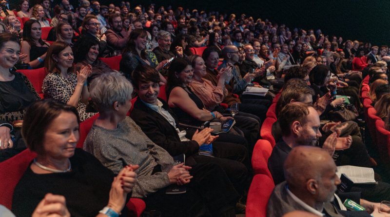 Público lleno en las butacas rojas del cine durante los APAs del año pasado, aplaudiendo y sonriendo. Imagen: AudioUK