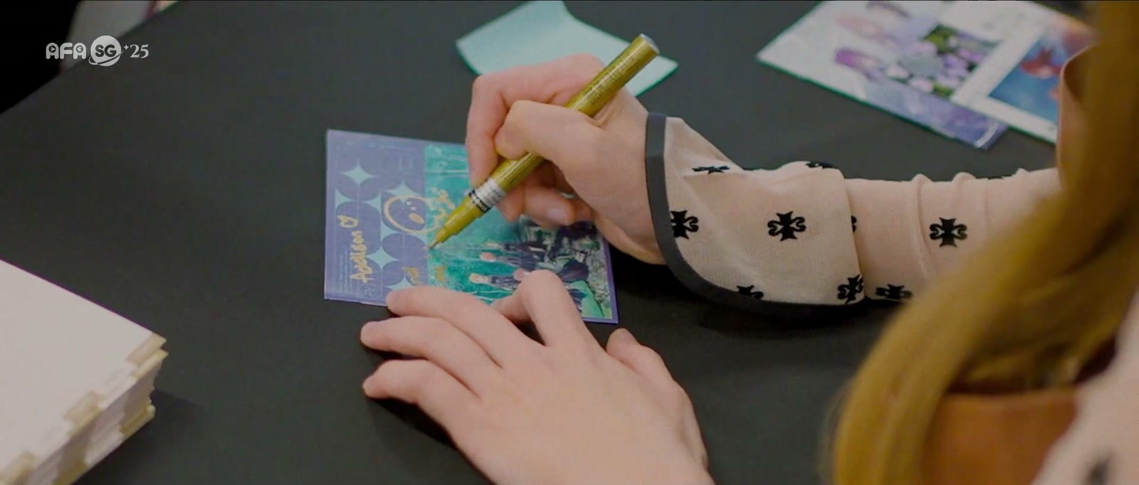 A guest signs a card with a gold pen at a meet and greet table during AFA Singapore 2025, a frame from the festival's official highlights video. Image: Anime Festival Asia
