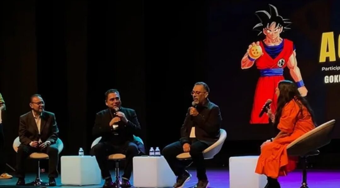 Mario Castañeda, Mario Arvizu y Mario Filio sentados en el escenario del Gimnasio Moderno de Bogotá con la directora Gaby Cárdenas micrófono en mano y Gokú en la pantalla, en el 7.º Festival Viva Voz. Imagen: Festival Viva Voz