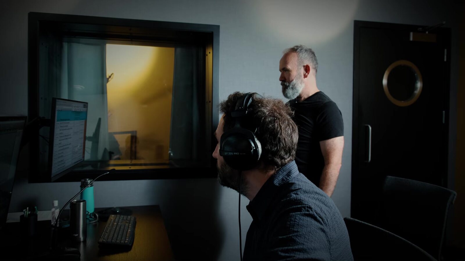 Two men in a control room watch through a window into the booth during the Valor Mortis sessions, with the voice director standing behind the engineer. Image: Lyrical Games, frame from the official behind-the-scenes film