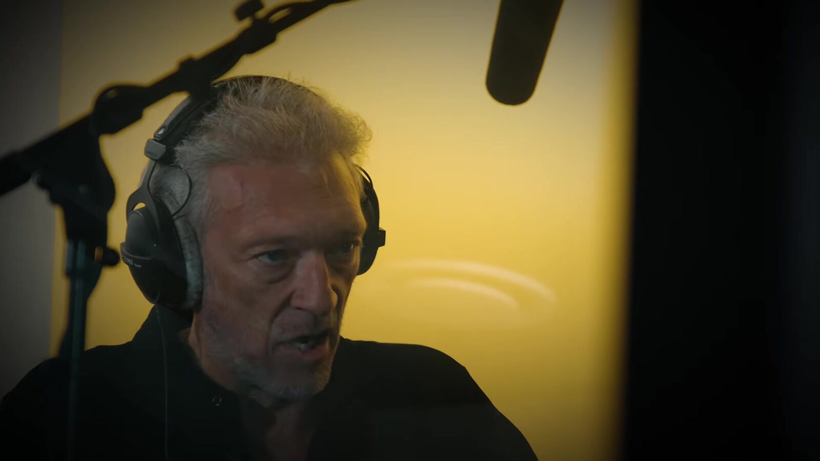 Vincent Cassel in headphones in front of a boom microphone during a Valor Mortis recording session, lit in yellow. Image: Lyrical Games, frame from the official behind-the-scenes film