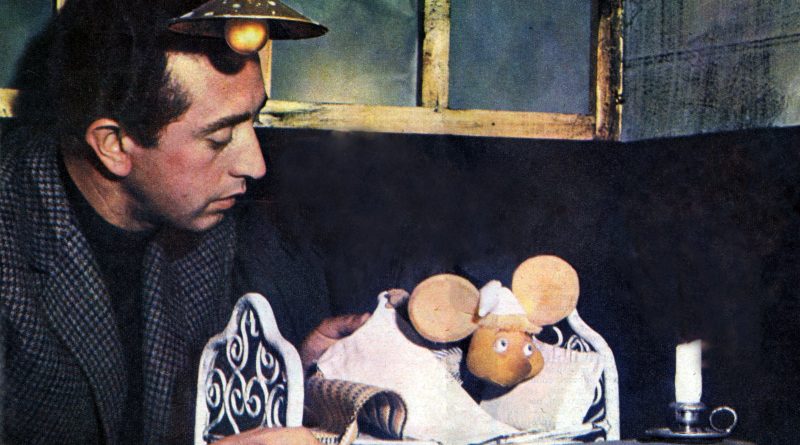 Peppino Mazzullo en 1961, con saco de tweed, inclinado sobre una cama en miniatura donde el títere de Topo Gigio está acostado junto a una vela. Imagen: Radiocorriere, 1961, dominio público