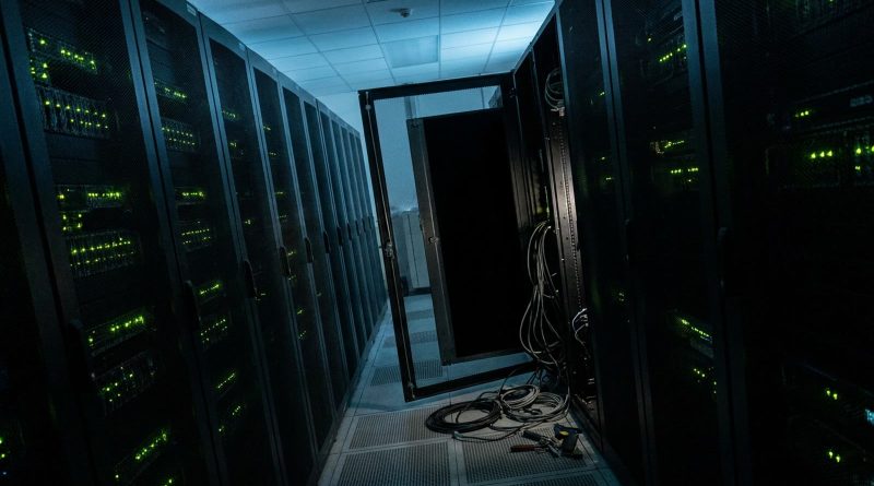 A data centre aisle at night with one server rack switched off, its door open and cables unplugged on the floor. © Voice Over Herald