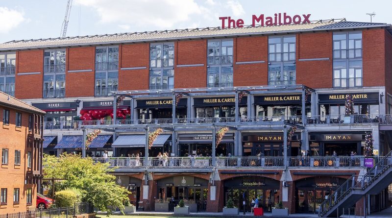The Mailbox en Birmingham, un edificio de ladrillo rojo con el letrero The Mailbox en el techo, sobre restaurantes junto al canal. Foto: The wub, CC BY-SA 4.0, vía Wikimedia Commons