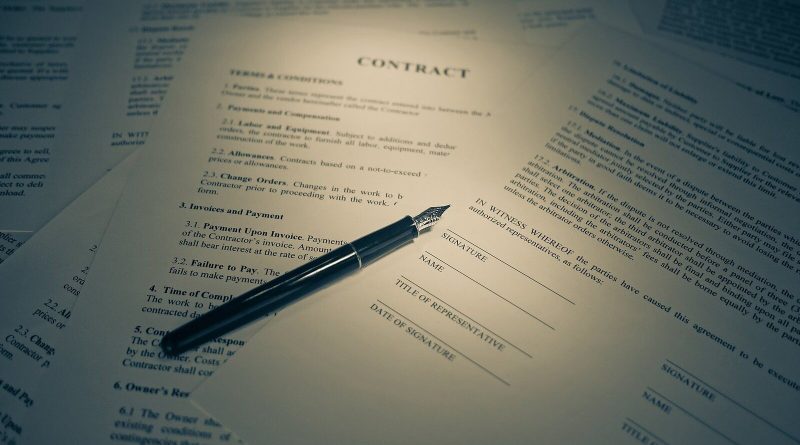 Contract pages spread across a desk under a warm lamp, the top page headed CONTRACT, with a black fountain pen resting beside the signature lines. Image: Blogtrepreneur (howtostartablogonline.net), CC BY 2.0, via Wikimedia Commons