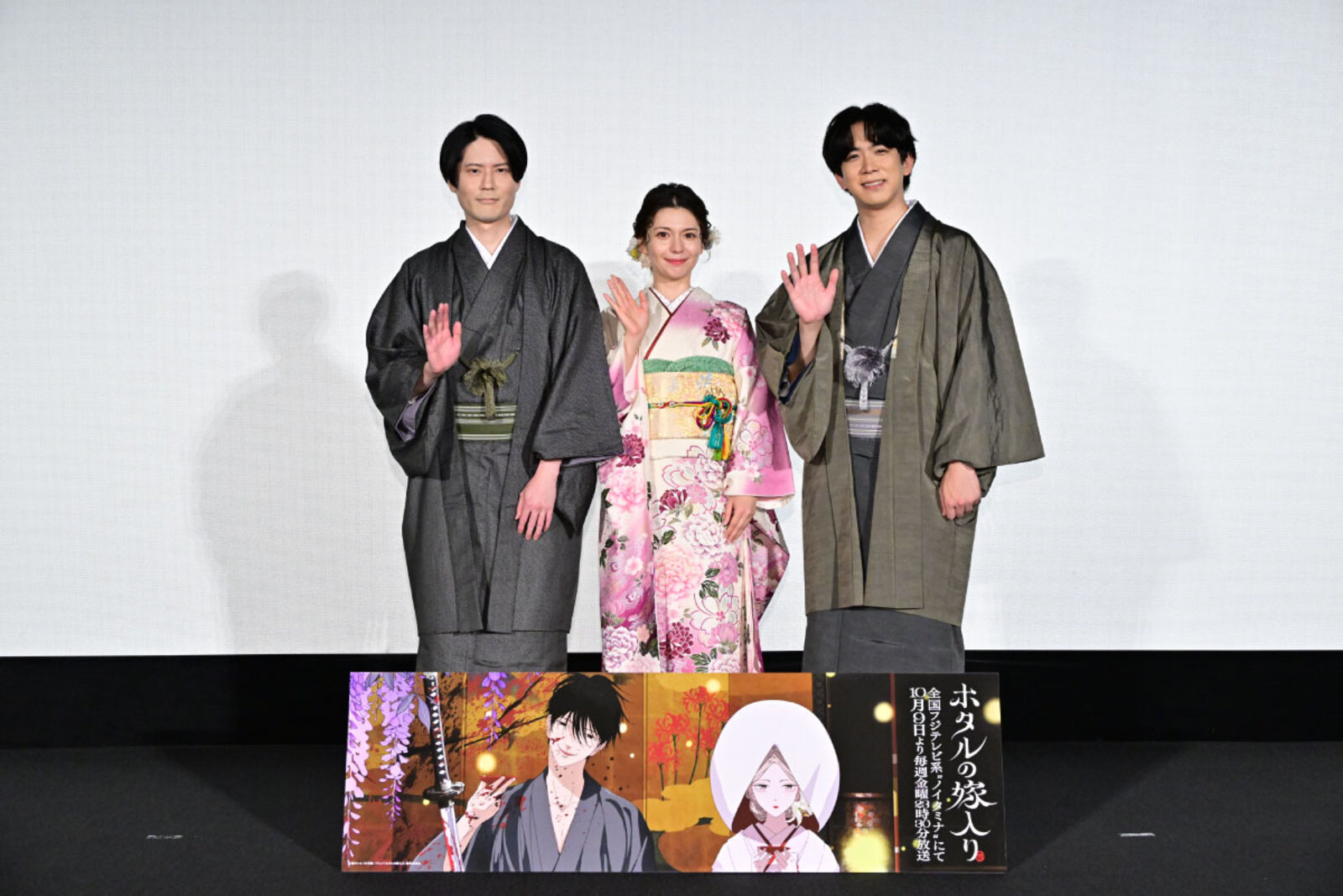 Lynn, con un furisode rosa de flores, entre Koki Uchiyama y Kent Ito, ambos con kimono oscuro, saludan en el escenario sobre un cartel de Firefly Wedding en la función anticipada en Tokio el 6 de septiembre de 2026. Imagen: sitio oficial del anime Firefly Wedding