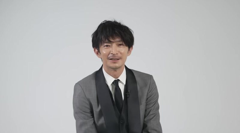 Kenjiro Tsuda, in a grey suit, smiling during a Netflix Anime interview. Image: Netflix Anime