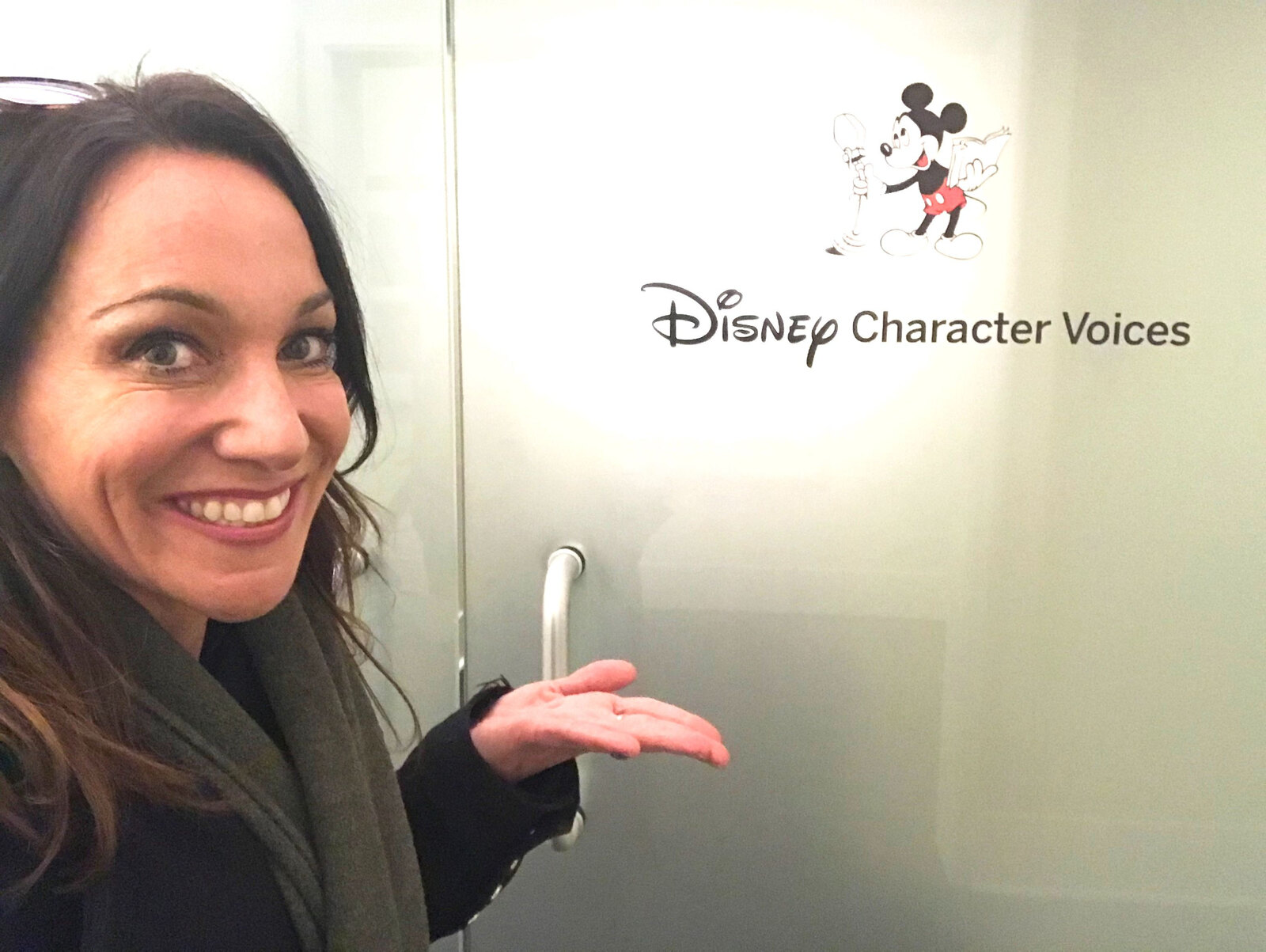 Laurie Burke sonríe junto al cartel de Disney Character Voices en la puerta esmerilada de un estudio, en una selfi. Foto: Laurie Burke