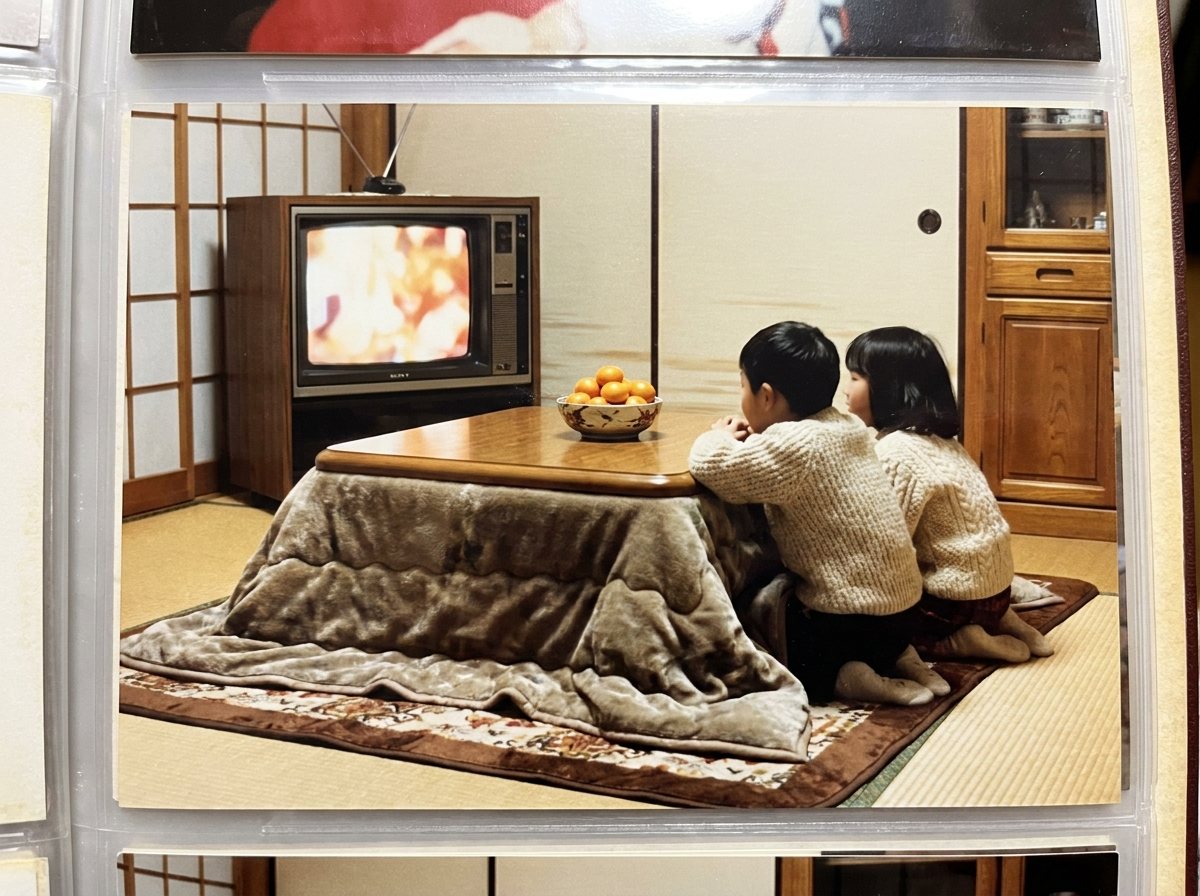 An old family snapshot in a photo album: two children in sweaters lean on a kotatsu table to watch a boxy TV in a tatami room © Voice Over Herald