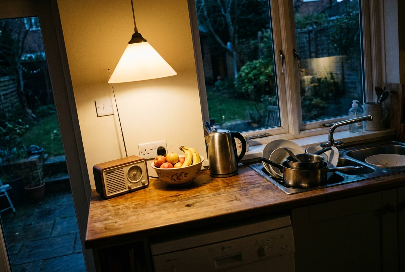 A family kitchen in the evening with a small radio on the counter beside a fruit bowl and a kettle. © Voice Over Herald
