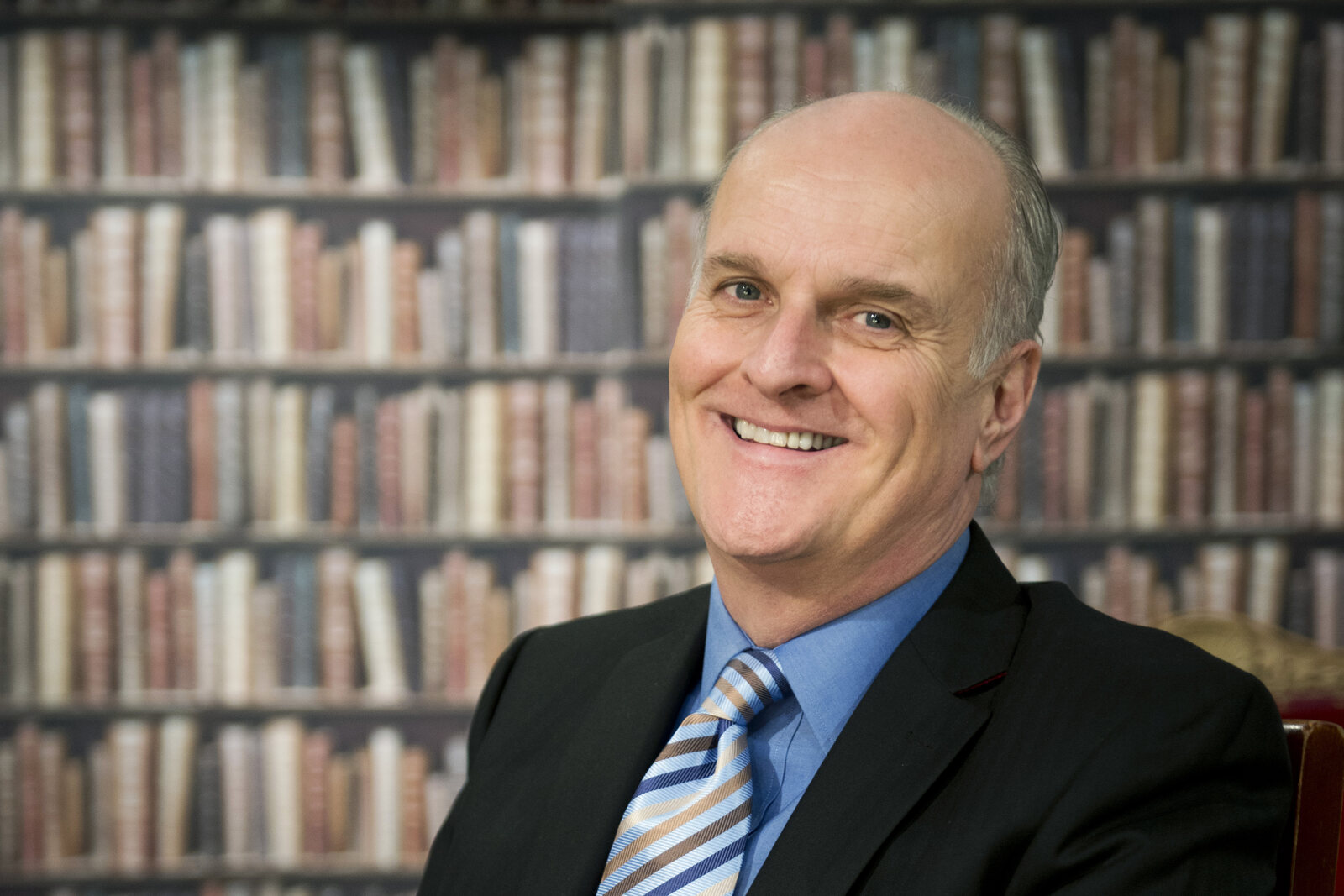 Peter Dickson sonríe de traje frente a estantes de libros antiguos. Imagen: kit de prensa de Peter Dickson