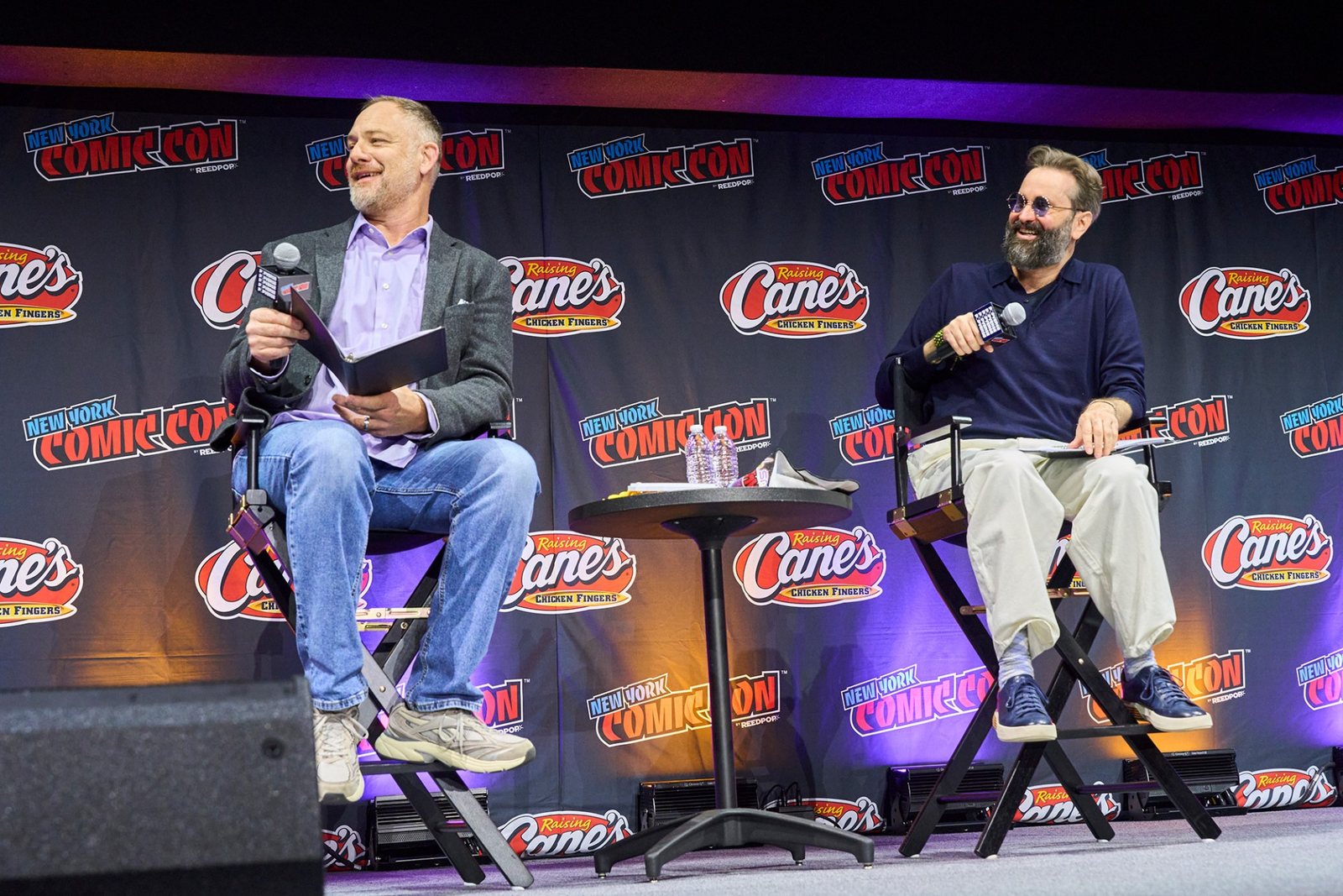 English dub actors Jason Douglas and Ian Sinclair seated on stools on the New York Comic Con stage, one holding a microphone and a clipboard. Image: Toei Animation, ©BIRD STUDIO/SHUEISHA, TOEI ANIMATION