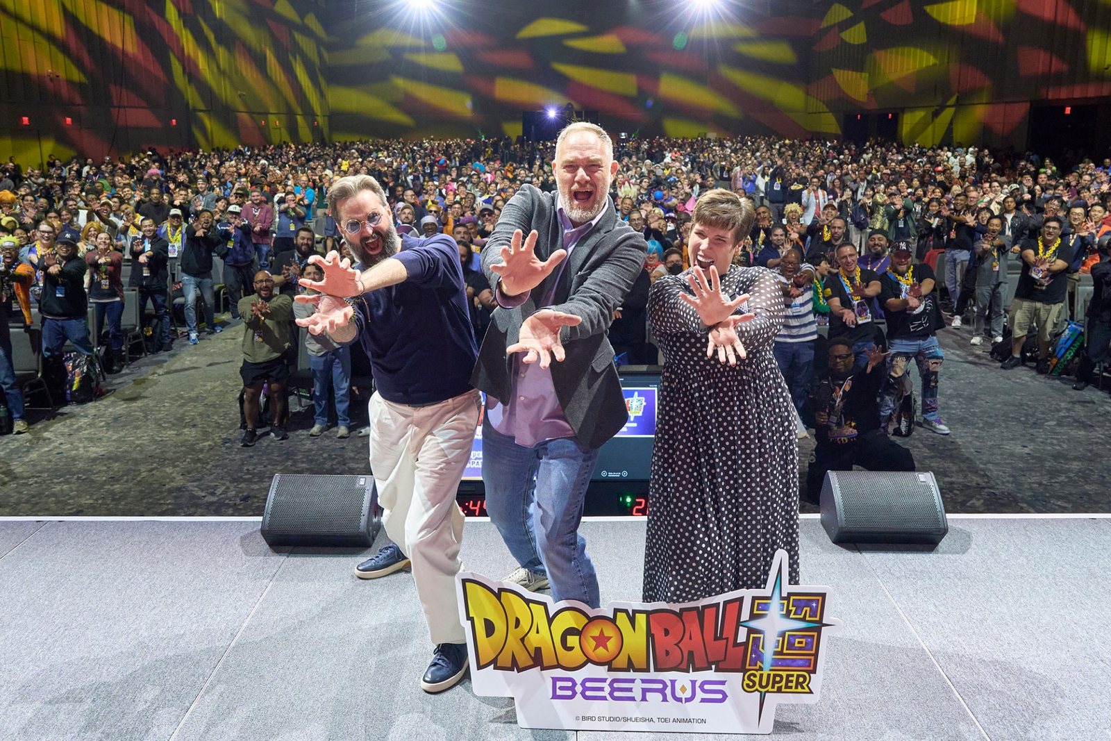 The three English dub panel guests strike a Kamehameha pose in front of the New York Comic Con crowd, with the Dragon Ball Super: Beerus sign at their feet. Image: Toei Animation, ©BIRD STUDIO/SHUEISHA, TOEI ANIMATION