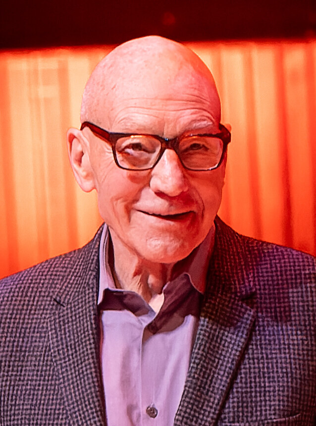 Patrick Stewart in glasses and a tweed jacket on stage at the Royal Festival Hall in London in October 2023. Image: Raph_PH, CC BY 2.0, via Wikimedia Commons
