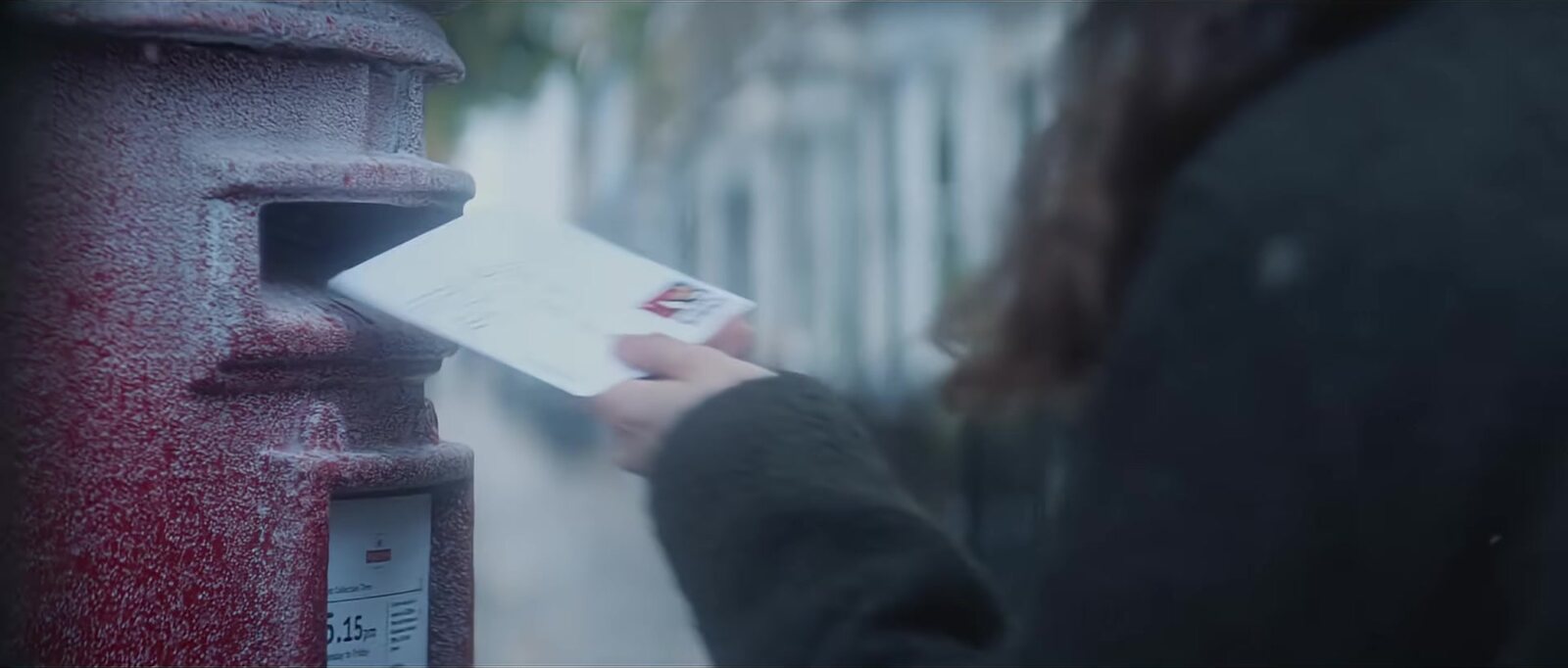 Una mano deposita una tarjeta en un buzón rojo cubierto de escarcha, escena del anuncio navideño 2025 de Royal Mail filmada con actores reales. Imagen: Royal Mail