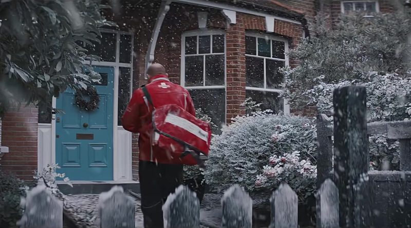 A Royal Mail postman in a red jacket walks up a snowy front path to a blue door, a frame from Royal Mail's 2025 Christmas ad. Image: Royal Mail