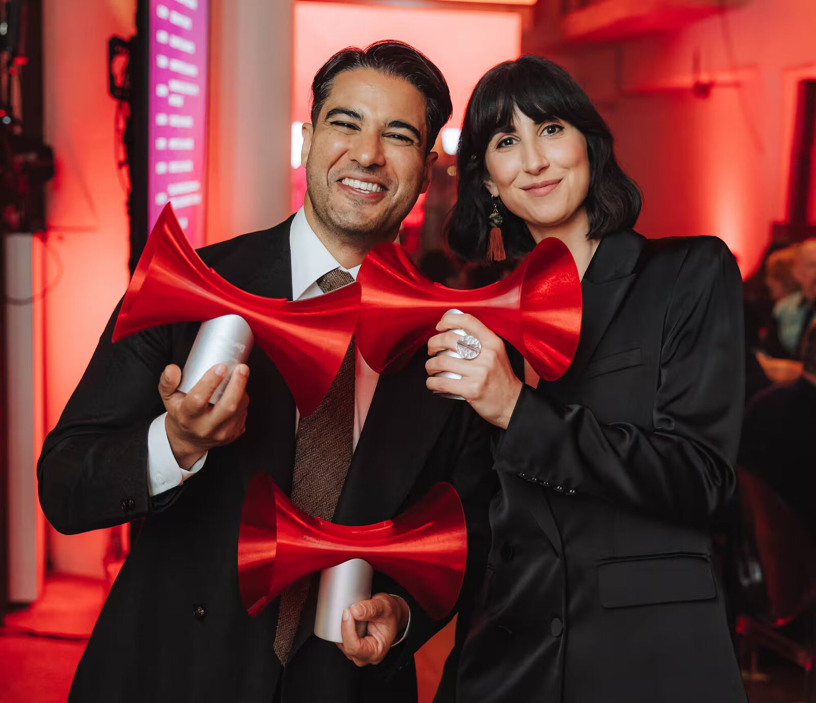 Marc Fennell smiles holding three red horn-shaped SONARR trophies beside a guest holding a fourth, at Machine Hall in Sydney. Image: SONARR Awards