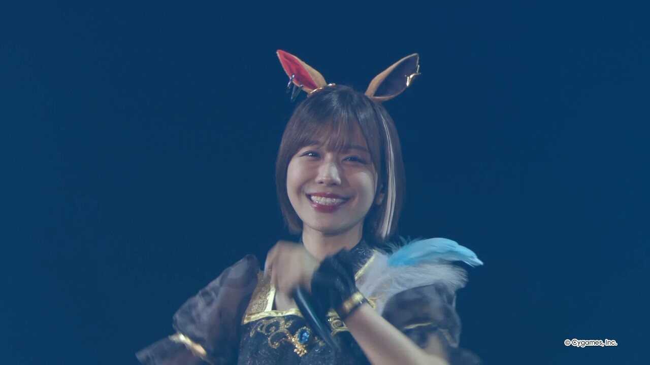 Una artista con vestuario de chica caballo, orejas y capa de plumas sonríe en el escenario de THE STAGE en Tokio, junio de 2026. Imagen: Cygames, vía The Television