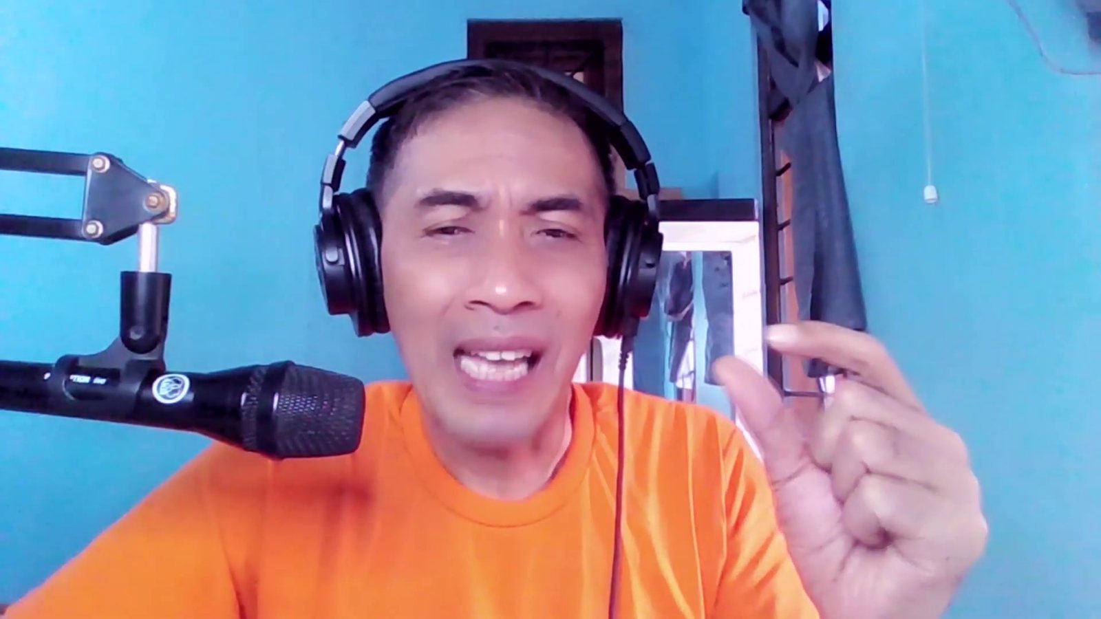 Toto Warsito explains a point with his hand raised, headphones on, at a microphone in his Belajar Dubbing lesson. Image: Toto Warsito, PAKDE TO on YouTube