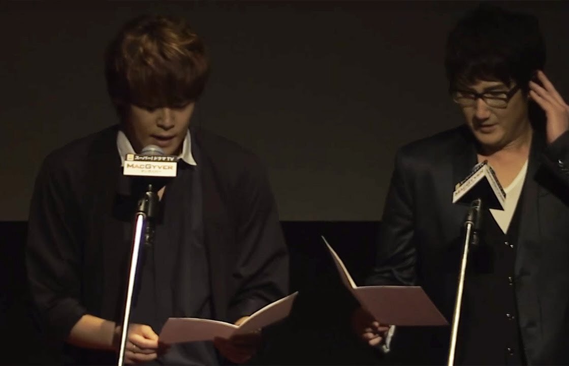 Mamoru Miyano, a la izquierda, y Hiroshi Tsuchida, a la derecha, leen sus guiones frente a los micrófonos durante un doblaje japonés en vivo de la serie MacGyver en 2017. Imagen: MANTAN, MAiDiGi TV
