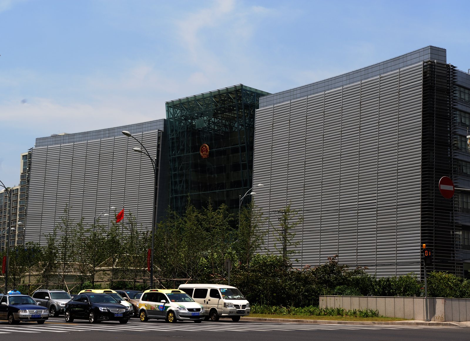 The glass and grey louvred facade of the Shanghai High People's Court on a sunny day, with taxis passing in front. Photo: Pyzhou, GFDL