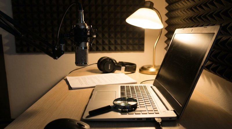 Un escritorio de estudio casero con micrófono, portátil y una lupa. © Voice Over Herald